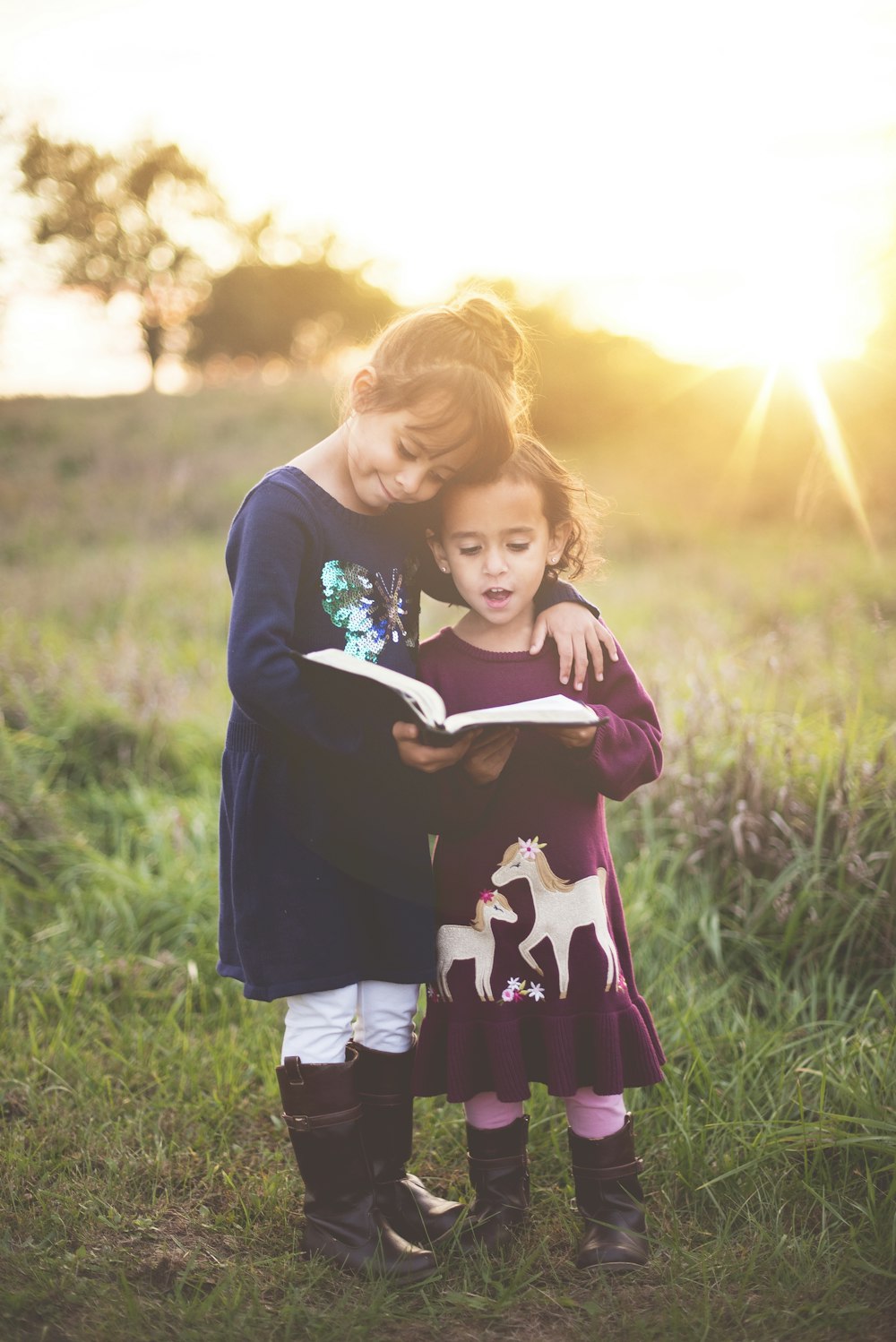 girl's left hand wrap around toddler while reading book during golden hour