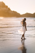 selective focus photo of woman standing on sea shore near rock formation during golden hour