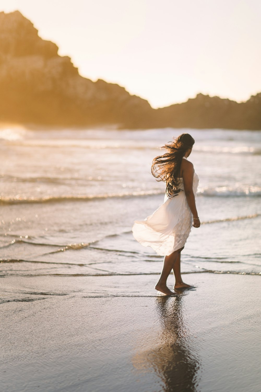 selective focus photo of woman standing on sea shore near rock formation during golden hour