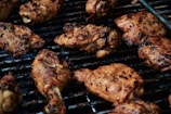 Several pieces of seasoned chicken are being grilled on a barbecue. The chicken pieces have a golden brown texture with visible grill marks, suggesting they are well-cooked.