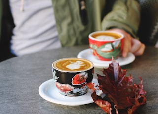 selective focus photo of black floral cup on white saucer with latte