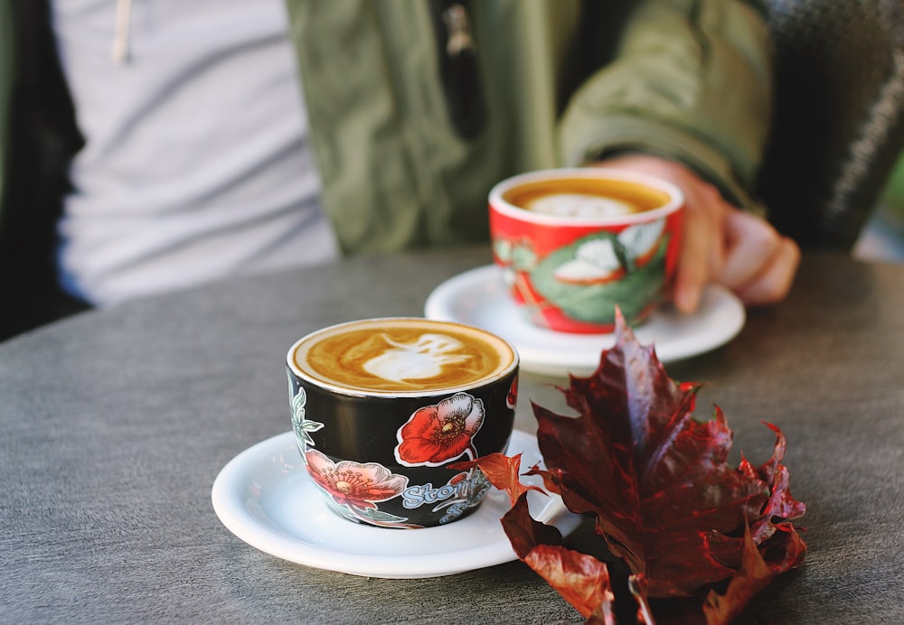 Photo de mise au point sélective d’une tasse florale noire sur une soucoupe blanche avec un café au lait