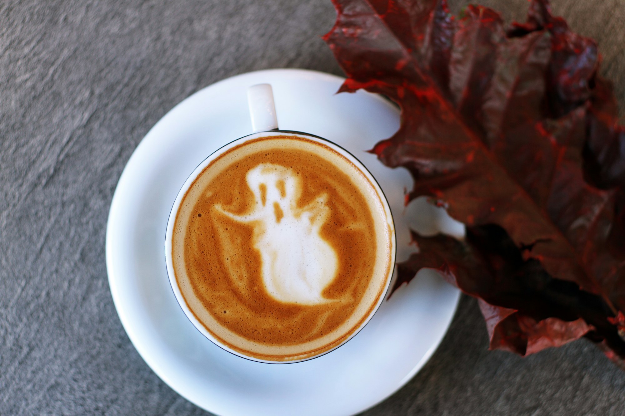 Coffee cup latte with art depicting a ghost for Halloween and pumpkin spice season.
