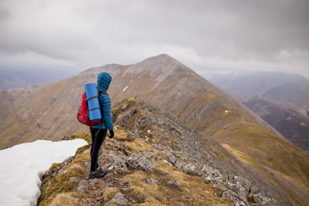 Person auf dem Gipfel des Berges trägt roten Rucksack