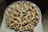 A round tray filled with small pastries, each topped with a piece of walnut. The pastries have a golden-brown crust and appear to include a dark filling, possibly a fruit or chocolate. The tray is placed on a light-colored surface.