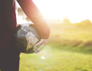 person holding black and brown globe ball while standing on grass land golden hour photography
