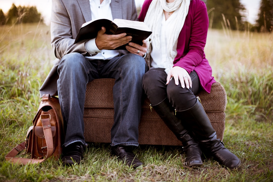 two people sitting beside each other, Man reading book on ottoman