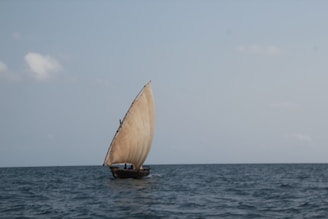 Traditional Omani dhow boat sailing peacefully along the Muscat coastline under a bright blue sky.