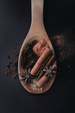 A wooden spoon resting on a kitchen counter next to a bowl of fresh herbs and spices.