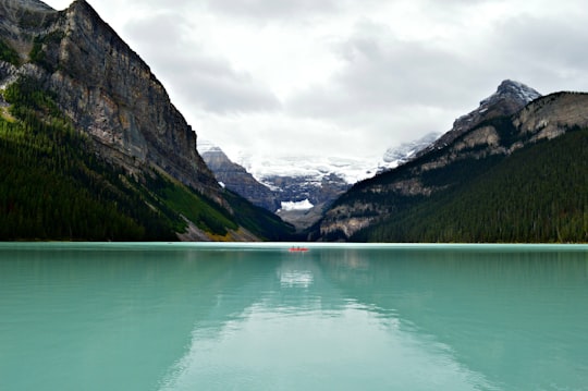 person riding on canoe boat in between hill on body of water in Banff National Park Canada