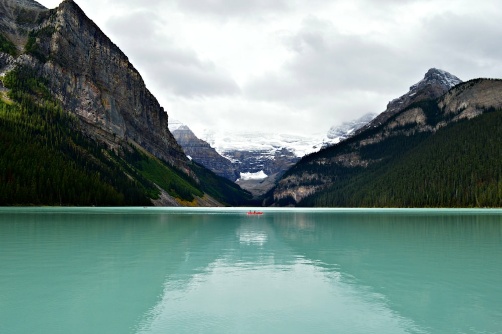 person riding on canoe boat in between hill on body of water