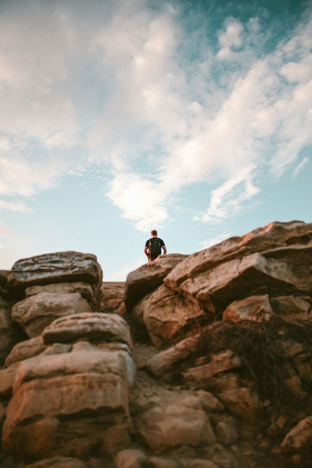 昼間、澄み切った青空の下、茶色の崖の上に立つ男のローアングル写真