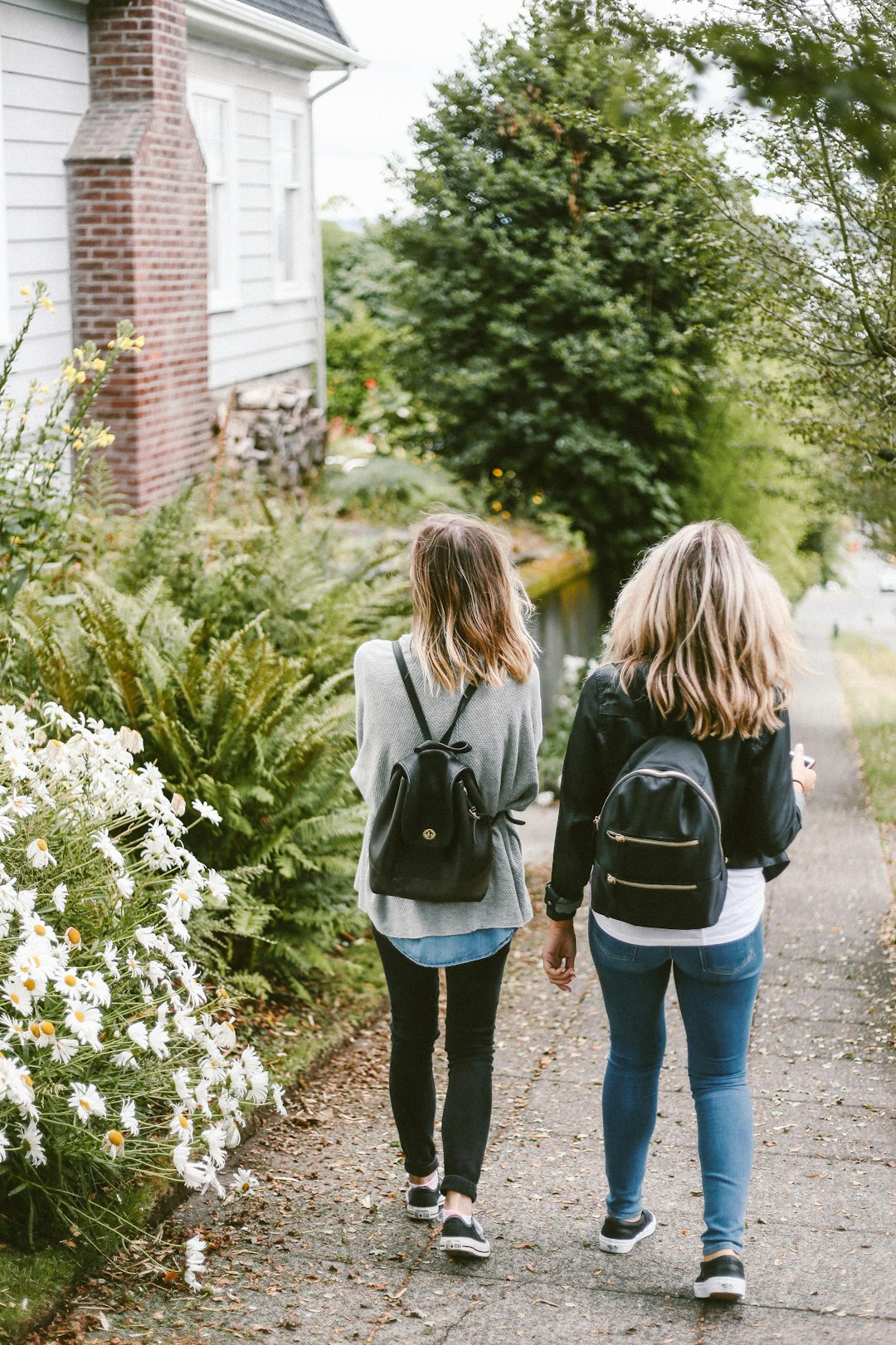 two ladies walking on sidewalk with black backpacks