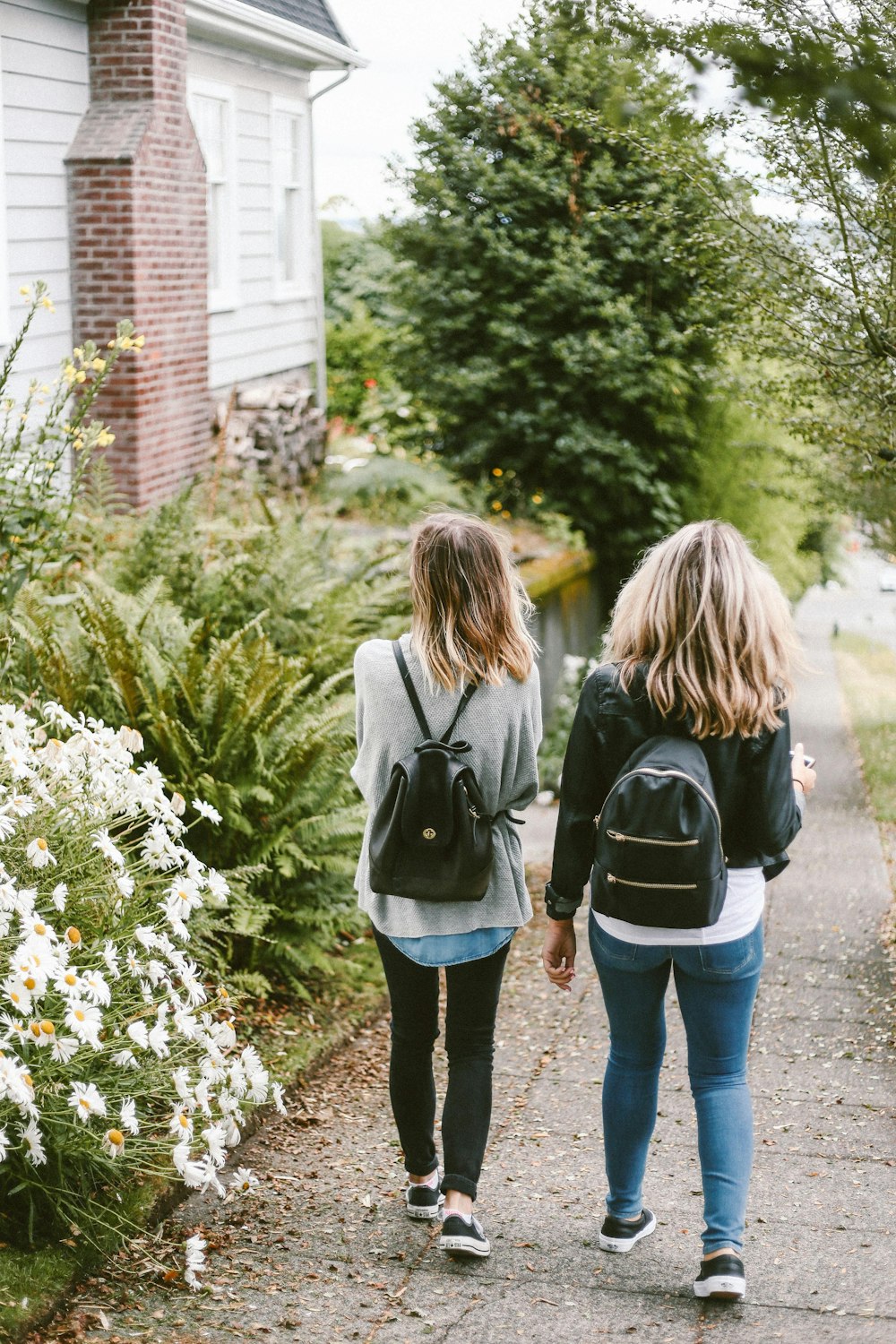 two ladies walking on sidewalk with black backpacks