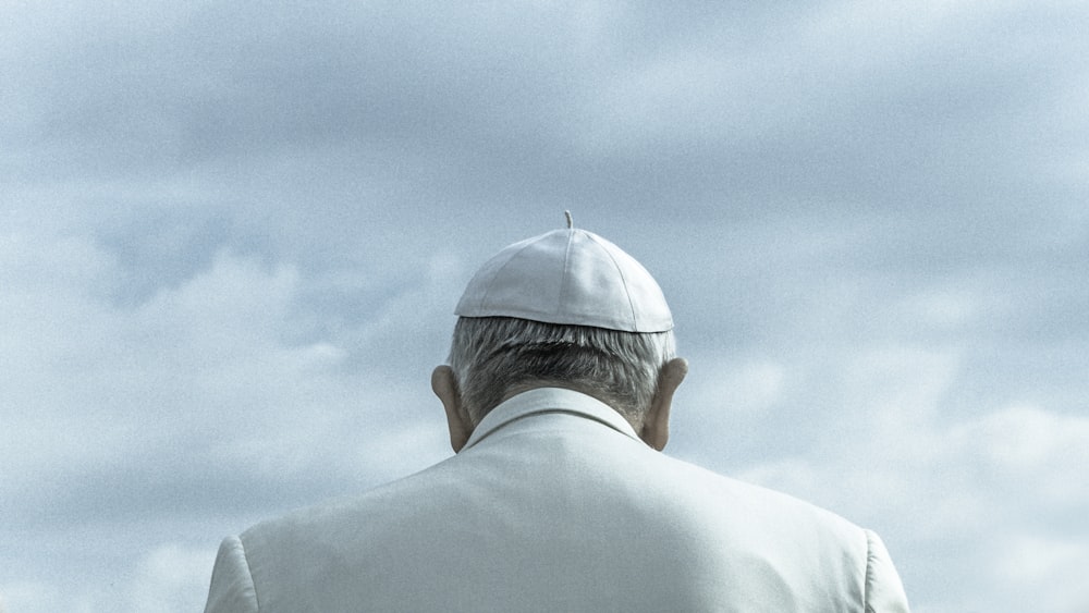 person wearing white cap looking down under cloudy sky during daytime