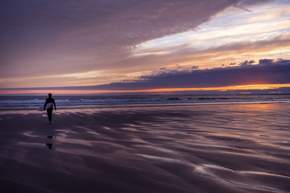 person standing on coastline under cloudy sky