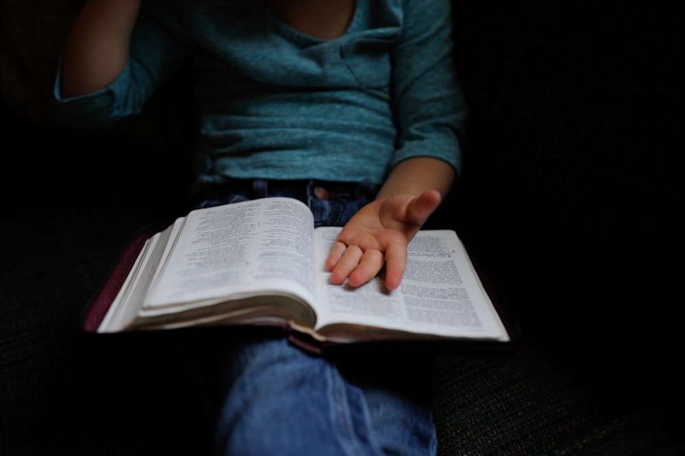 person wearing blue long-sleeved shirt reading book