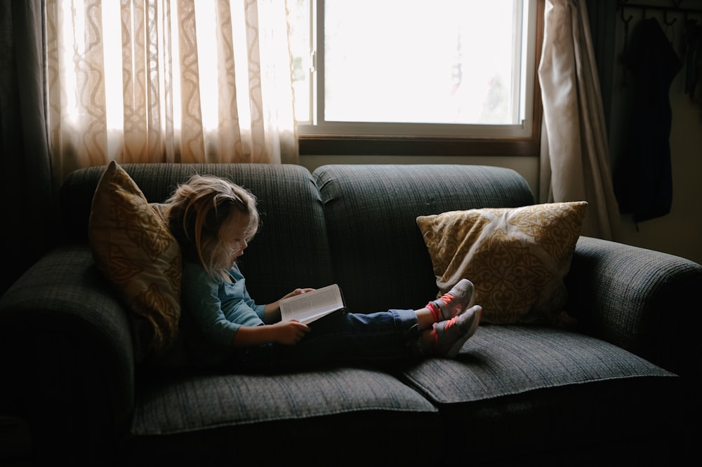 Mädchen, das ein Buch liest, sitzt auf dem Sofa