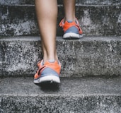 person wearing orange and gray Nike shoes walking on gray concrete stairs