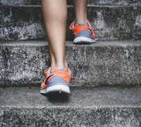 person wearing orange and gray Nike shoes walking on gray concrete stairs