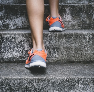 person wearing orange and gray Nike shoes walking on gray concrete stairs