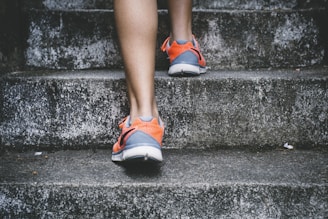 person wearing orange and gray Nike shoes walking on gray concrete stairs