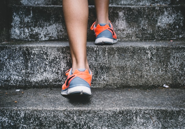 person wearing orange and gray Nike shoes walking on gray concrete stairs