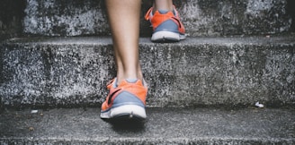 person wearing orange and gray Nike shoes walking on gray concrete stairs