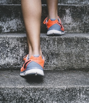 person wearing orange and gray Nike shoes walking on gray concrete stairs