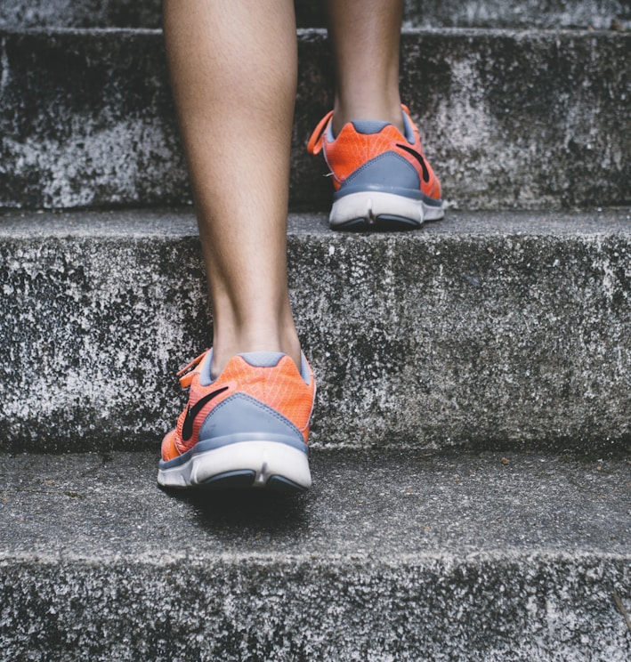 person wearing orange and gray Nike shoes walking on gray concrete stairs