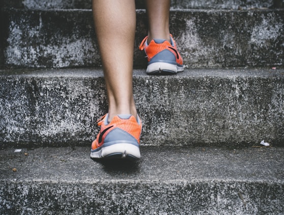 person wearing orange and gray Nike shoes walking on gray concrete stairs