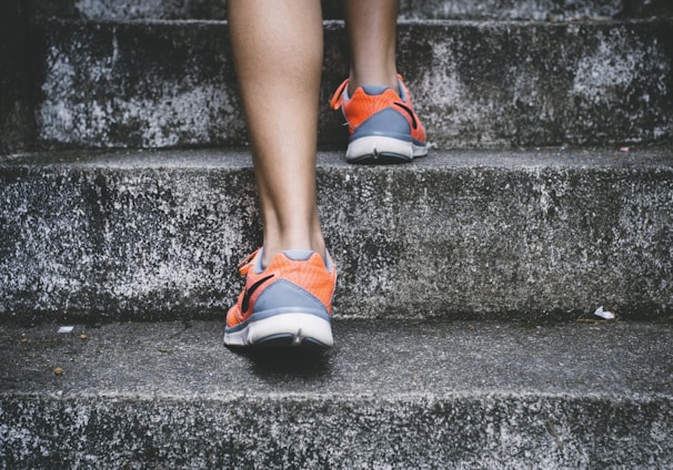 person wearing orange and gray Nike shoes walking on gray concrete stairs