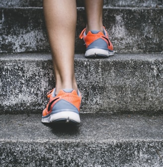 person wearing orange and gray Nike shoes walking on gray concrete stairs