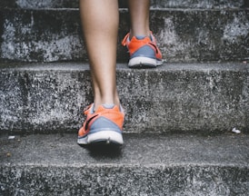 person wearing orange and gray Nike shoes walking on gray concrete stairs