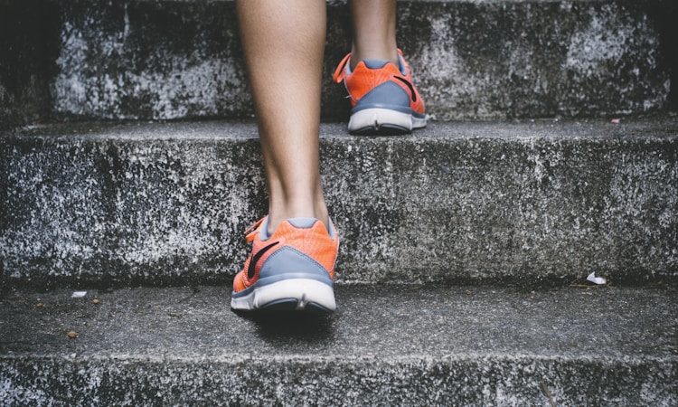 Person Wearing Orange And Gray Nike Shoes Walking On Gray Concrete Stairs