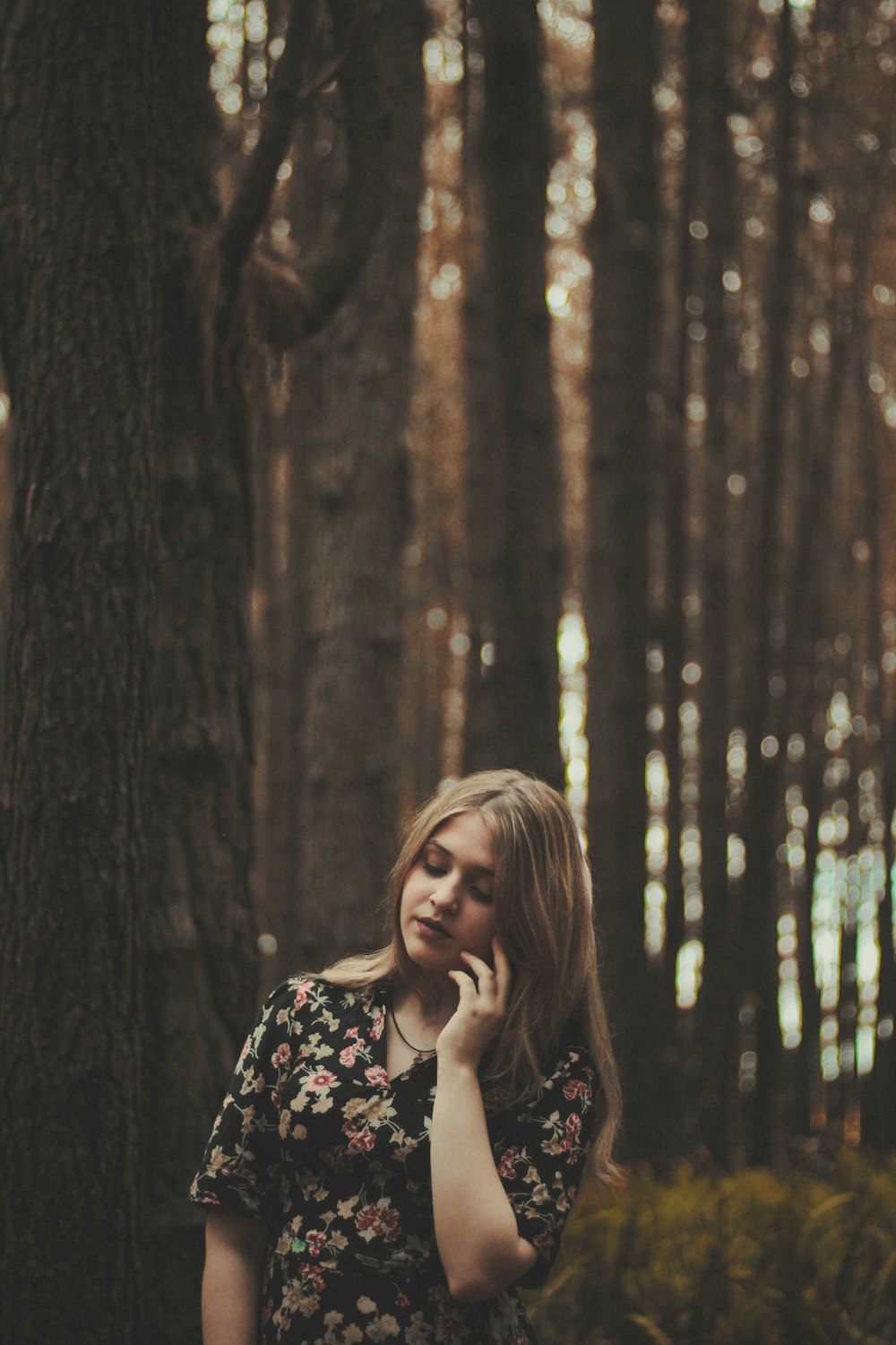 standing woman beside gray tree while holding left cheek during daytime