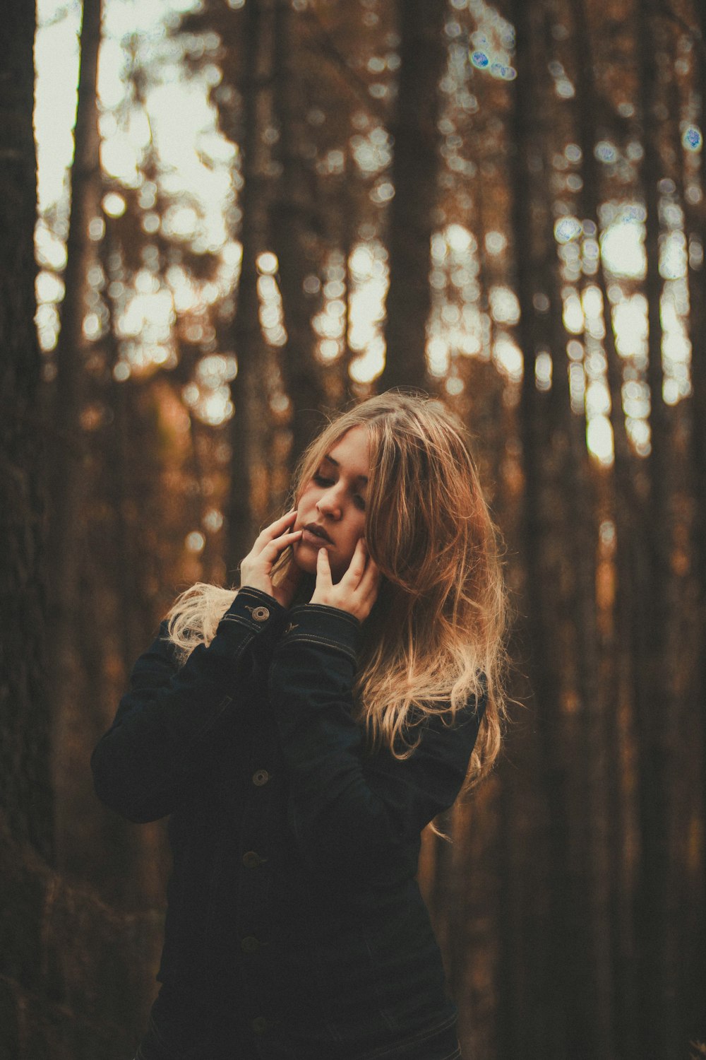 fotografia do retrato da mulher vestindo o casaco preto cercado por árvores da floresta durante o dia