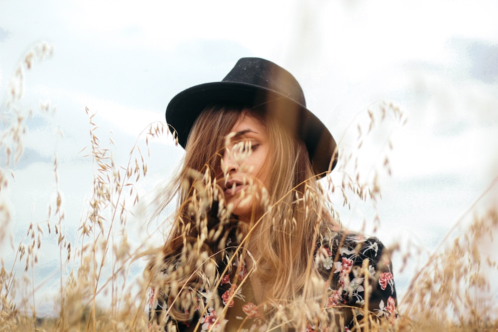 Mujer con sombrero negro cerca de la hierba marrón durante el día