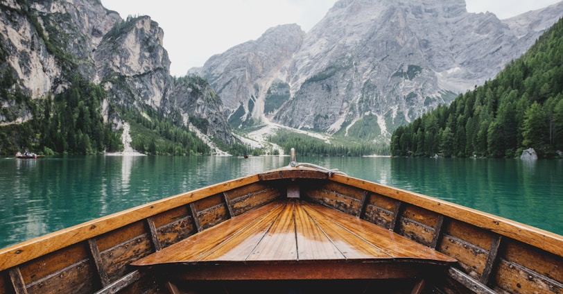 brown wooden boat moving towards the mountain