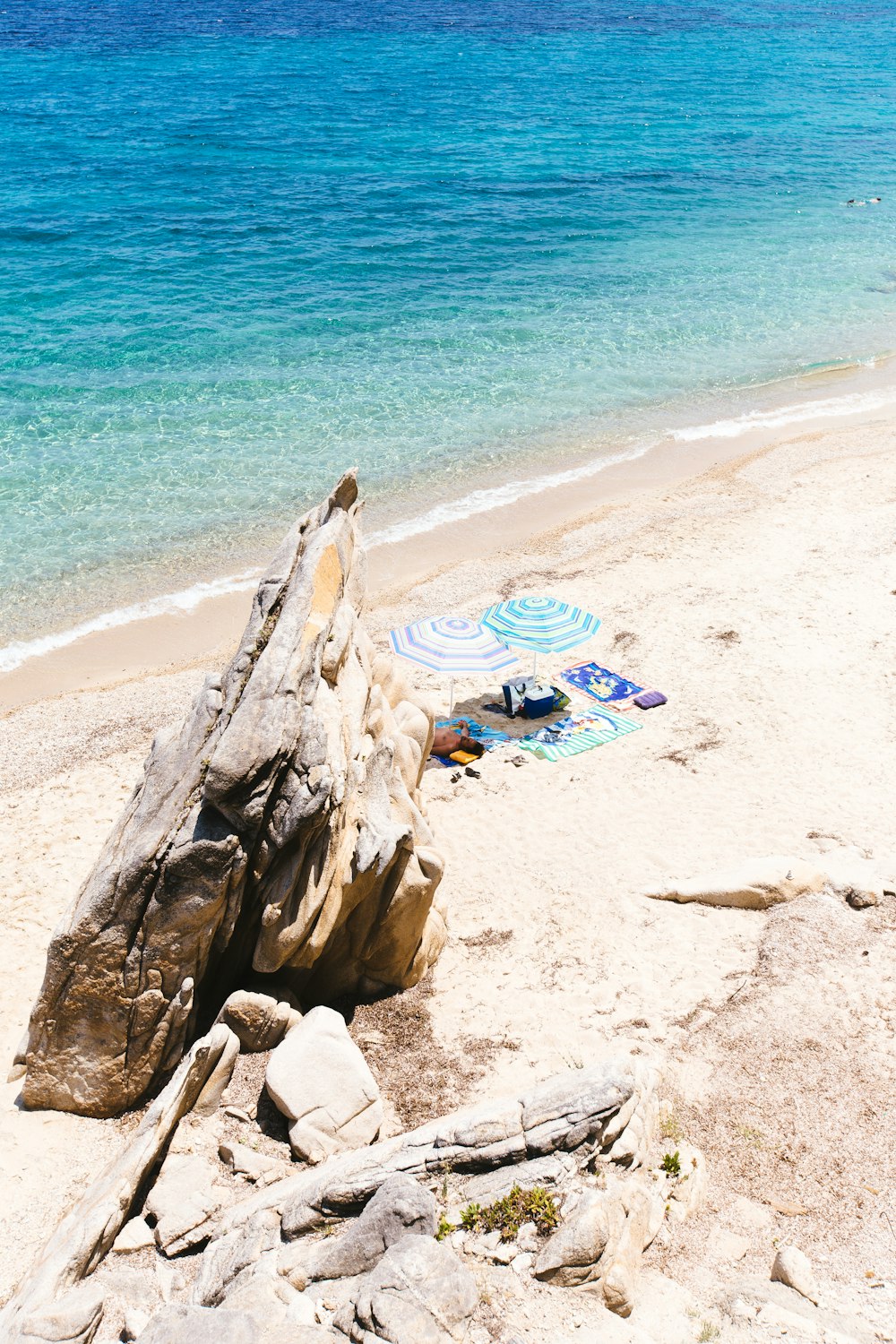 a rock on a beach with a blue umbrella in the background