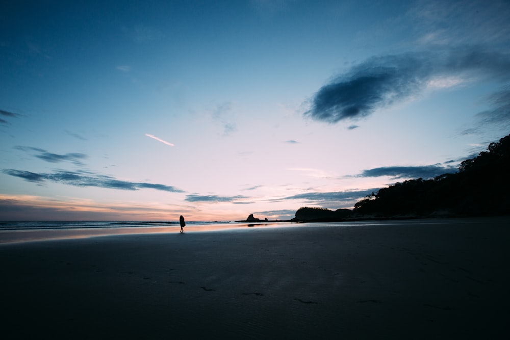 areia cinzenta ao lado do corpo de água durante o pôr do sol