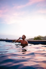 topless man drinking beverage while on swimming pool