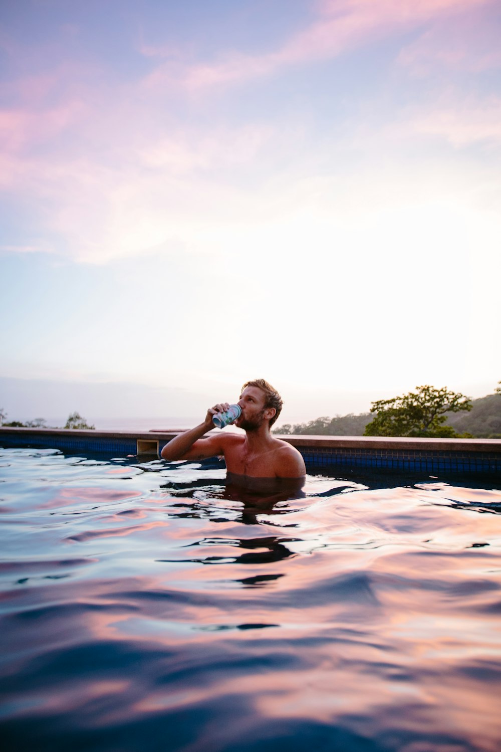 topless man drinking beverage while on swimming pool