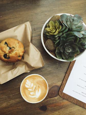 A warm wooden table set with a latte, green juice, berry smoothie, avocado panini, quinoa salad, and a blueberry muffin, bathed in soft natural light.