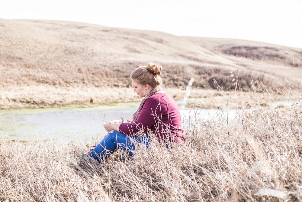 woman sitting on grass beside concrete road at daytime