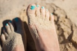 person sky-blue nail polish feet on brown sand