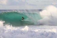 man riding surfboard under sea wave during daytime