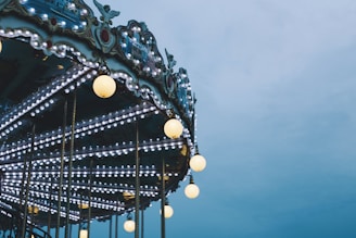 A carousel adorned with numerous bright lights and ornate decorative elements, set against a cloudy sky.