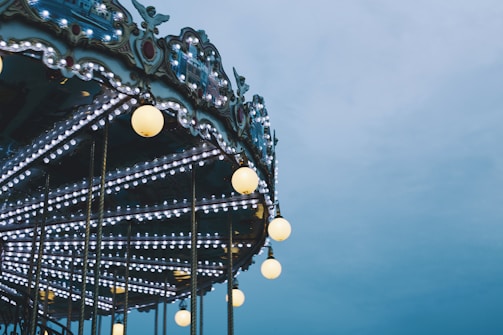 A carousel adorned with numerous bright lights and ornate decorative elements, set against a cloudy sky.