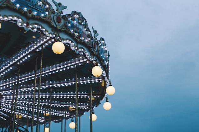A carousel adorned with numerous bright lights and ornate decorative elements, set against a cloudy sky.